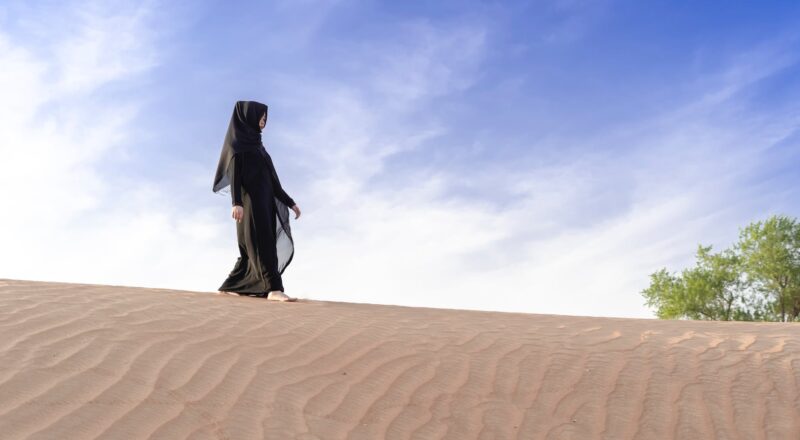 photo of woman wearing abaya while walking on desert